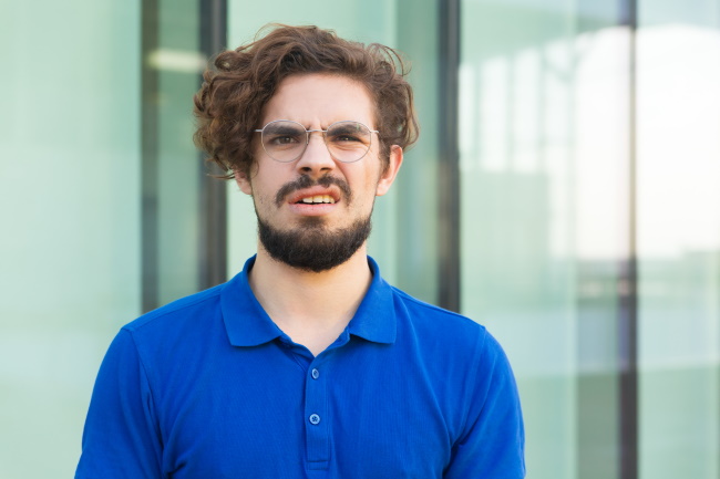 Bild von jungem mann mit braunen Locken und Brille, der die Augenbrauen nach oben zieht. Er macht den Eindruck, als würde er etwas nicht verstehen. Bild von jungem mann mit braunen Locken und Brille, der die Augenbrauen nach oben zieht. Er macht den Eindruck, als würde er etwas nicht verstehen.